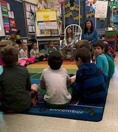 Students and teacher sit on a classroom floor